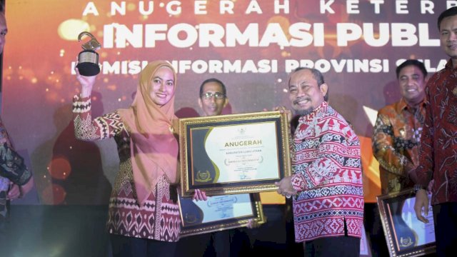 Bupati Luwu Utara Indah Putri Indriani saat menerima penghargaan terbaik ke dua se Sulawesi Selatan dalam hal keterbukaan informasi yang diserahkan pada malam Anugerah Keterbukaan Informasi Publik 2022 di Claro Hotel Makassar malam kemarin Jumat (02/12/2022).